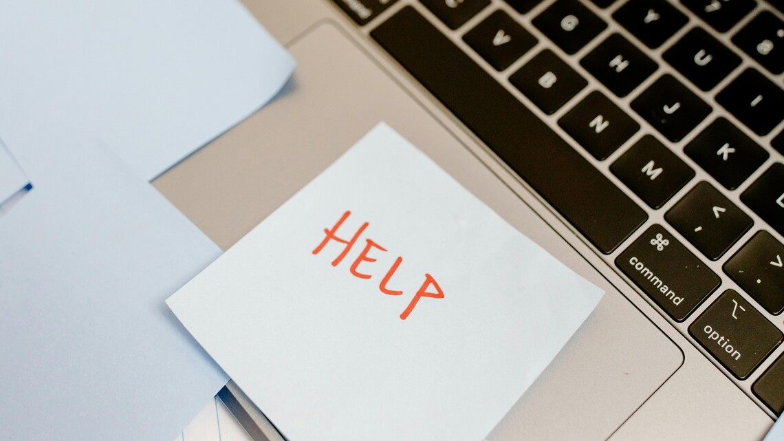 a sticky note with the word 'help' stuck to the track pad of a laptop