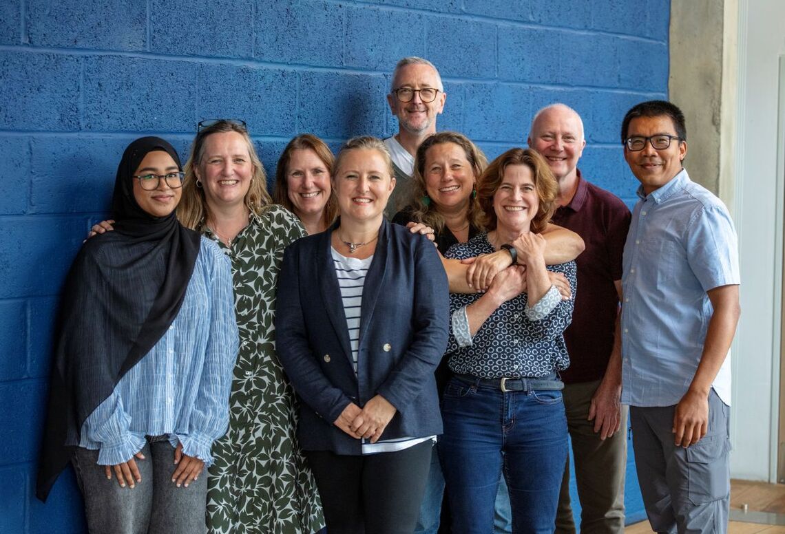 Superhighways team members stood together in a row against a blue backdrop. We're close together, sometimes arms linking and smiling