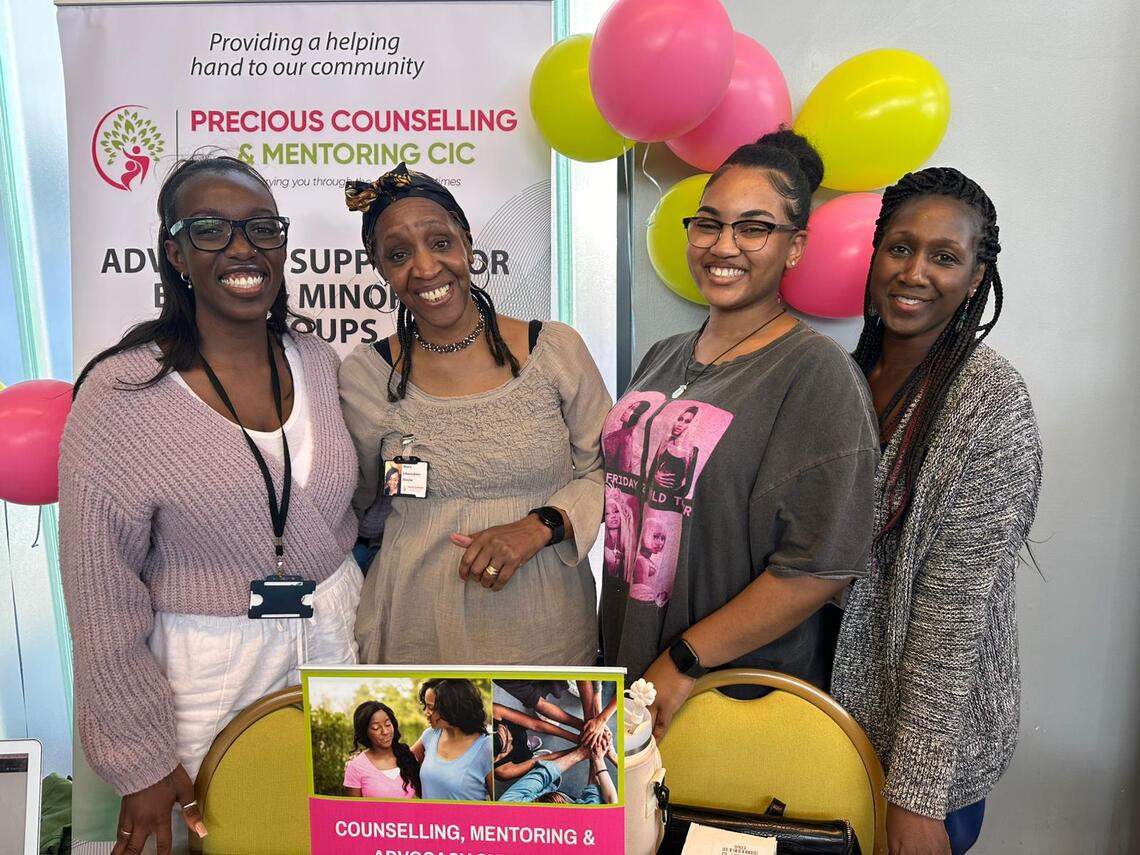four members of precious counselling and mentoring standing in front of banner and balloons and smiling